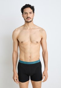 Fekete boxeralsó, kék elasztikus derékpánttal, amelyen a "BJÖRN BORG" felirat található. Az anyag sima és jól illeszkedő. A modellen atlétikus testalkat látható.