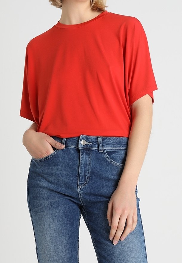 Top rosso a maniche corte realizzato in un tessuto liscio, abbinato a jeans in denim azzurro chiaro con chiusura a bottone e tasche frontali.