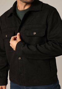 Veste en daim noir avec un devant à boutons, deux poches poitrine et des manches longues. Comprend un col et une texture lisse.