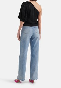 Schwarzes Top mit einem Schulterträger und strukturiertem Stoff, kombiniert mit hellblauen weitem Jeans mit fransigem Saum und leuchtend pinken High Heels.