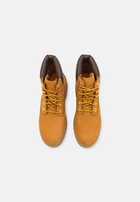 Botas de tornozelo castanhas e amarelas em material de camurça, ponta redonda, gola acolchoada e atacadores amarelos contrastantes em ilhós castanhos.