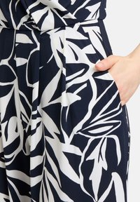 Tessuto blu navy con un motivo botanico di foglie bianche; presenta una tasca laterale; texture liscia e design strutturato con pieghe.
