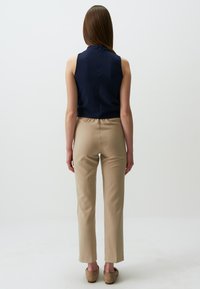 Top senza maniche blu navy con tessuto testurizzato, abbinato a pantaloni beige slim-fit con cintura elastica e taglio alla caviglia. Calzature marroni visibili.