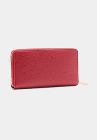 Piros bőr pénztárca texturált felülettel, cipzáras zárral és aranyszínű fémrészletekkel. Téglalap alakú, sima körvonallal.