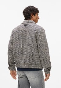 Vævet jakke i en blanding af marineblå, creme og grå, med krave, lange ærmer og ribbet kant. Brandinglabel på ryggen.