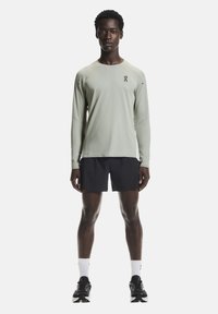 Maglietta sportiva a maniche lunghe di colore verde chiaro abbinata a pantaloncini neri. Presenta un logo discreto sul petto e una vestibilità atletica standard.