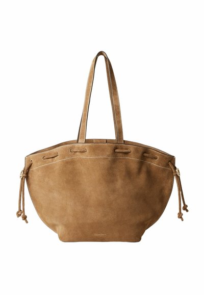 Bolso tote de ante marrón con doble asa, detalles de cordón en los lados y costura blanca visible en el borde superior.