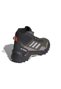 Stivale da trekking verde scuro e grigio con tomaia texturizzata, suola in gomma nera, strisce bianche prominenti e linguetta rossa sul tallone.