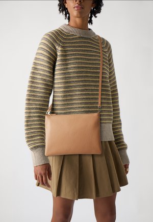 Borsa a tracolla in pelle color beige con finitura testurizzata, forma rettangolare e design sottile, indossata con un maglione a righe e una gonna plissettata.