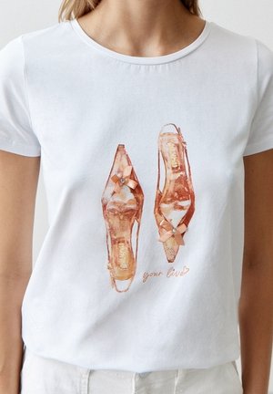 T-shirt blanc avec un motif imprimé de deux chaussures à talons hauts en or rose ornées de petits nœuds et la phrase "your live" en dessous.