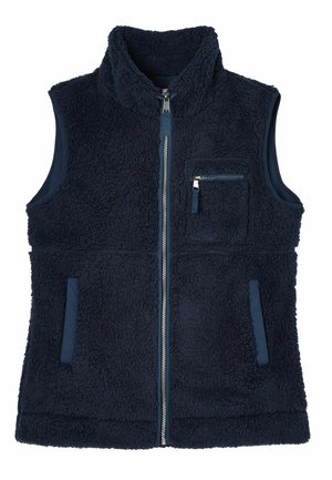 Navy fleece vest over a striped long-sleeve shirt, light blue jeans, cream sneakers, and a pink knit beanie. Soft textures and casual fit.