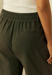 Donkergroene joggers met een elastische tailleband, voorzien van een subtiele textuur en een enkele achterzak met een gestikte rand.