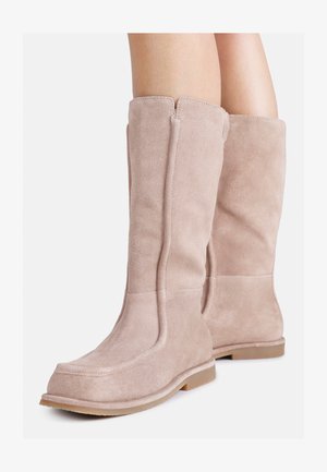 Čizmice do koljena od svijetloružičastog nubuka s mekom teksturom, koja se odlikuje glatkim siluetom i ravnim, fleksibilnim potplatom. Bez vidljivih metalnih elemenata ili uzoraka.