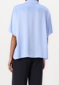 Svetle modrá hedvábná košile s krátkým rukávem a límečkem, volného střihu a hladké textury, doplněná tmavými kalhotami.