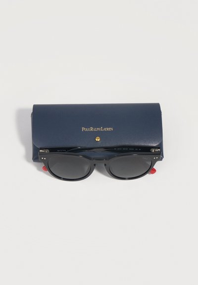 Black sunglasses with dark lenses resting on a navy blue Polo Ralph Lauren case with gold lettering and snap closure.