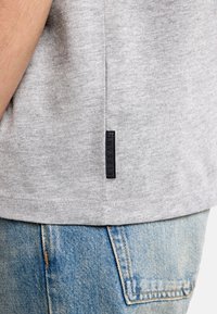 Šedé bavlnené tričko s krátkymi rukávmi a bočnou značkou. Skombinované s modrými džínsovými šortkami s vyblednutým, textúrovaným vzorom.