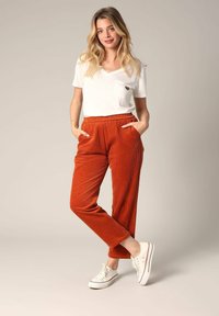 Witte V-hals t-shirt met een zak, gecombineerd met oranje corduroy broek met een elastische tailleband en zijzakken, gedragen met witte sneakers.