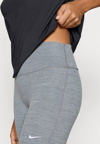 Γκρι αθλητικό κολάν με ψηλή μέση, με ομαλή υφή και διακριτικό σχέδιο heather, και μικρό λογότυπο Nike σε λευκό στο πλάι.