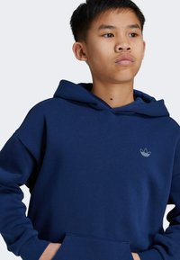 Sudadera de color azul marino hecha de una tela suave, con un bolsillo delantero, capucha con cordón y un pequeño logo blanco en el pecho. Textura suave, corte relajado.