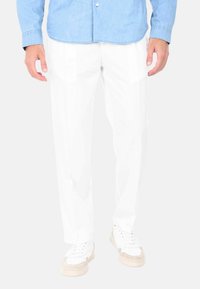 Pantaloni bianchi realizzati in tessuto leggero, con taglio dritto, gamba leggermente affusolata e tasche laterali; indossati con sneakers bianche.
