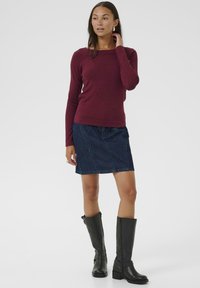 Bordeaux lange mouwen top met een vierkante halslijn, gecombineerd met een donkere denim rok en kniehoge zwarte leren laarzen met een gestructureerde afwerking.
