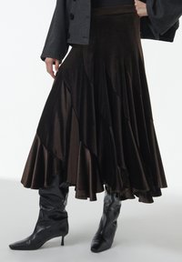 Falda de terciopelo marrón en capas con una silueta fluida y un dobladillo con volantes, combinada con botas negras brillantes hasta la rodilla.