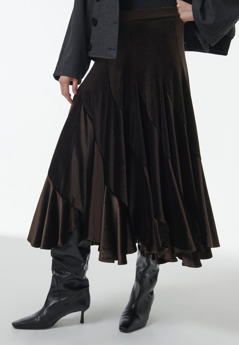 Falda de terciopelo marrón en capas con una silueta fluida y un dobladillo con volantes, combinada con botas negras brillantes hasta la rodilla.