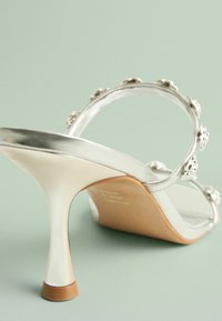 Silver höga klacksandaler med en glänsande finish, som har ett tunt band med blommor och en beige-tonad formad sula.
