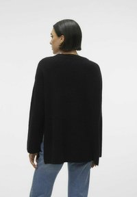 Maglione oversized nero realizzato in tessuto lavorato a maglia, caratterizzato da un ampio scollo, maniche lunghe e una vestibilità morbida che arriva ai fianchi.