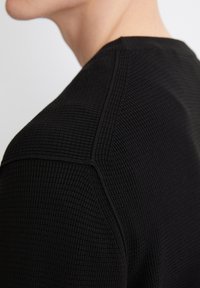 Schwarzes, strukturiertes Hemd mit geriffeltem Muster, Rundhalsausschnitt und sichtbaren Nähten entlang der Schulternaht.