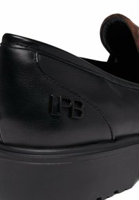 Chaussures noires en cuir à enfiler avec un accent brun texturé et une semelle noire moulée. Présente le logo 'LPB' en relief sur le côté.