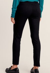 Pantalons noirs skinny avec une texture lisse, poches arrière et taille mi-haute, associés à un pull turquoise et des mocassins noirs.