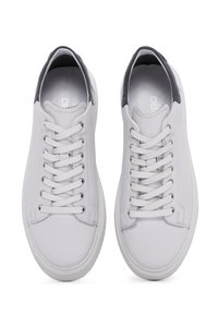 Zapatillas de cuero blancas con un diseño de corte bajo, punta redonda, cordones blancos y un acento trasero en navy contrastante. Textura suave, detalles de costura simples.