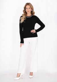 Pulover negru cu mânecă lungă, cu o margine albă, purtat cu pantaloni albi lărgi și tocuri albe cu vârful ascuțit. Texturi netede vizibile.