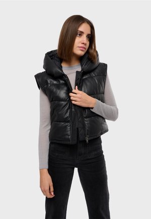 Gilet sans manches noir avec capuche, présentant une fermeture éclair et un motif matelassé. Porté par-dessus un haut à manches longues gris clair et un pantalon noir.