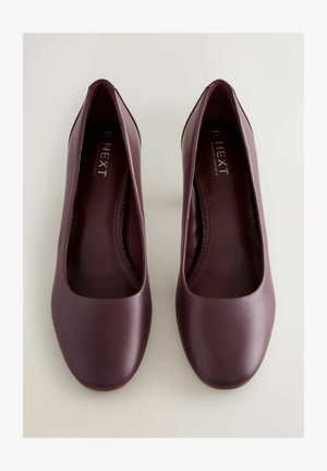 Burgundi színű, alacsony sarkú cipők sima bőrfelülettel, kerek orral és egyszerű, letisztult dizájnnal. Nincs látható fémrész vagy minta.
