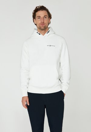 Weißer Kapuzenpullover mit einer Vordertasche, ausgestattet mit einem schwarzen Logo auf der Brust. Glatte Textur und gerippte Bündchen sowie Saum. Kombiniert mit dunklen Hosen.