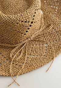 Chapeau en paille tressée à large bord avec un motif texturé et un nœud décoratif tressé noué autour de la base de la calotte.