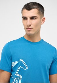 Blue cotton t-shirt featuring a white graphic of a horse with wings on the left side, round crew neckline, and short sleeves.