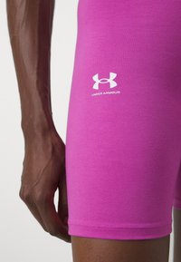 Růžové sportovní šortky z elastického materiálu, s bílým logem Under Armour na dolní části nohy a přiléhavým střihem.