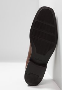 Braunes Leder-Schuh mit einer glatten Oberfläche, ausgestattet mit einer strukturierten schwarzen Gummisohle und einem klassischen Design mit detaillierter Stickerei.