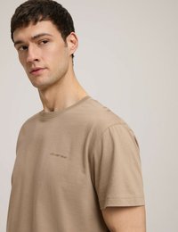 Beżowa koszulka bawełniana z krótkimi rękawami i okrągłym dekoltem. Posiada subtelne logo w tym samym kolorze na lewej stronie klatki piersiowej.