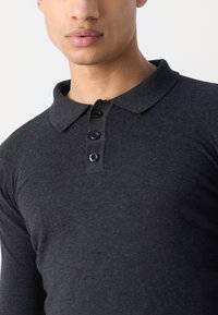 Sort langærmet polo-shirt lavet af blødt stof, med en krave og fire sorte knapper ned langs placket. Glat tekstur.