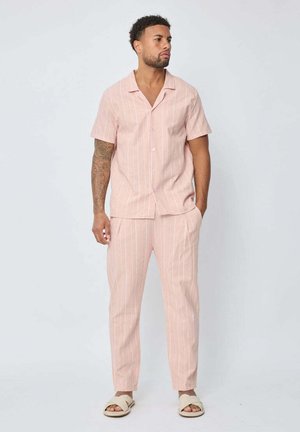 Chemise rose clair à manches courtes et pantalon assorti à rayures verticales. Le tissu est lisse, avec une fermeture à boutons et des poches latérales.