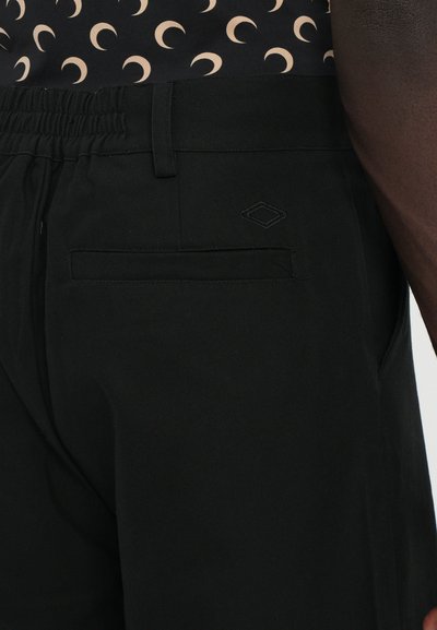 Black pants featuring an elastic waistband, tidy stitching, a back pocket, and a small diamond logo accent near the pocket. Smooth texture.