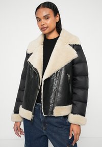 Schwarze Leder- und gepolsterte Steppjacke mit einem Kragen und Manschetten aus cremefarbenem Kunstfell. Verfügt über Reißverschlusstaschen vorne und hat ein kurzes Design.