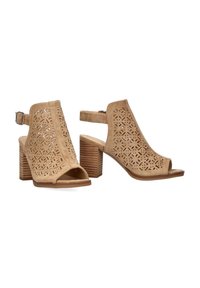 Zapatos beige de punta abierta con recortes geométricos, una correa en el tobillo y un tacón apilado. Están hechos de un material similar al ante con una suela plana.