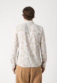 Pitkähihaista paitaa kevyestä beigeistä kankaasta, jossa on valkoinen palmunlehtikuvio, nappihihansuut ja kaareva helma. Sisältää perinteisen kauluksen.