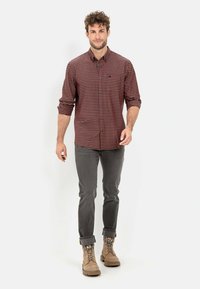 Red and black checked button-up shirt, gray slim-fit jeans, and beige lace-up boots with a textured surface and rolled cuffs.