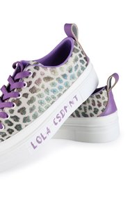 Vita sneakers med en lila leopardtryck på ovandelen, texturerad yta, lila snörning och en "LOLA CSDMNT"-tryck på sidan.